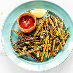 Kurkuri Bhindi arrange in a blue plate with a bowl of tomato ketchup and lemon wedge