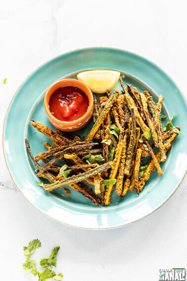 Kurkuri Bhindi arrange in a blue plate with a bowl of tomato ketchup and lemon wedge