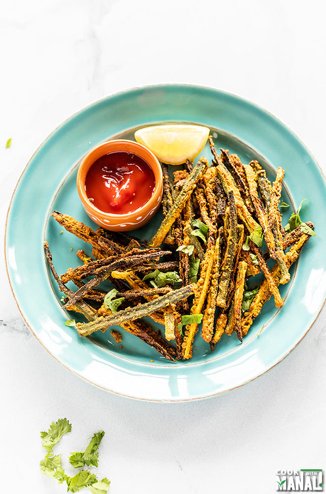 Kurkuri Bhindi arrange in a blue plate with a bowl of tomato ketchup and lemon wedge