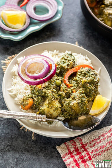 spinach curry served over white rice and garnished with sliced onion and lemon wedge