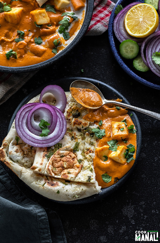 a plate of naan served with paneer butter masala and sliced onions along with a spoon