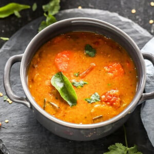 sambar served in a grey bowl garnished with curry leaves with twigs on cilantro and more curry leaves scattered all around