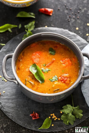 sambar served in a grey bowl garnished with curry leaves with twigs on cilantro and more curry leaves scattered all around