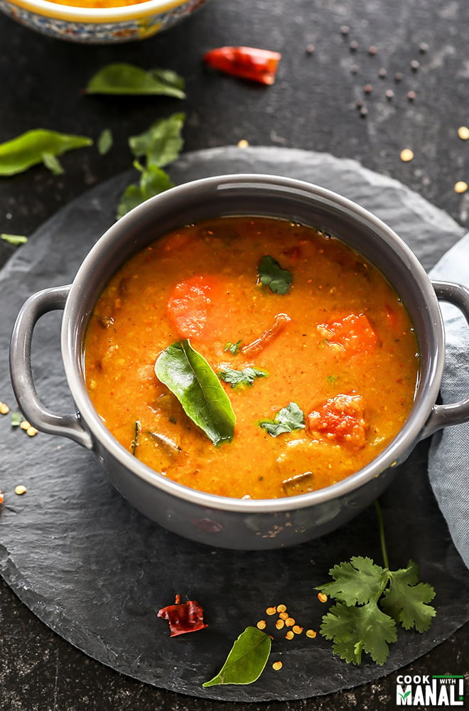 sambar served in a grey bowl garnished with curry leaves with twigs on cilantro and more curry leaves scattered all around