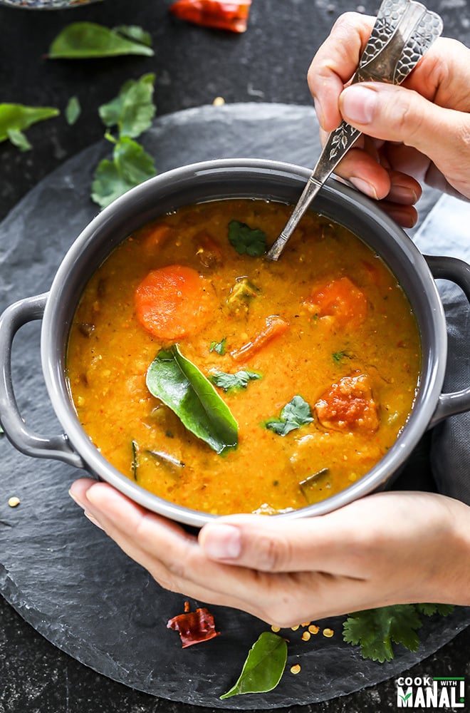 a hand digging into a bowl of sambar with a spoon