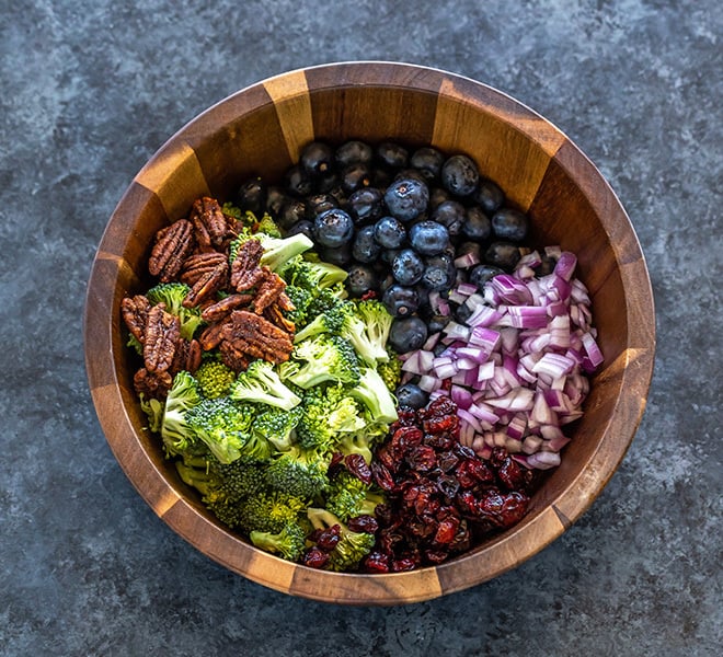 a salad bowl with chopped broccoli, onion, blueberries, pecans and dried cranberries