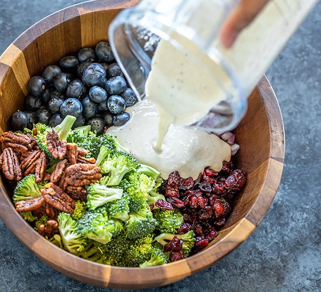 dressing being poured over a bowl of vegan broccoli salad