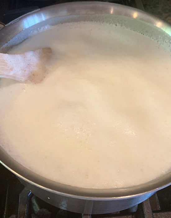 milk boiling in a steel pot with a wooden spatula stirring