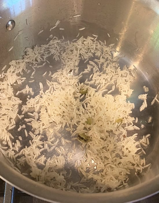 rice being sauteed in ghee in a steel pot