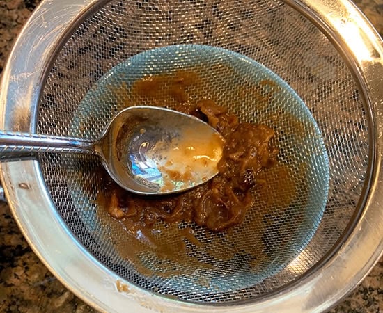 tamarind pulp being strained using a strainer with a spoon