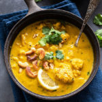 mango curry with cauliflower and cashews served in a black pan placed over blue napkin garnished with cilantro