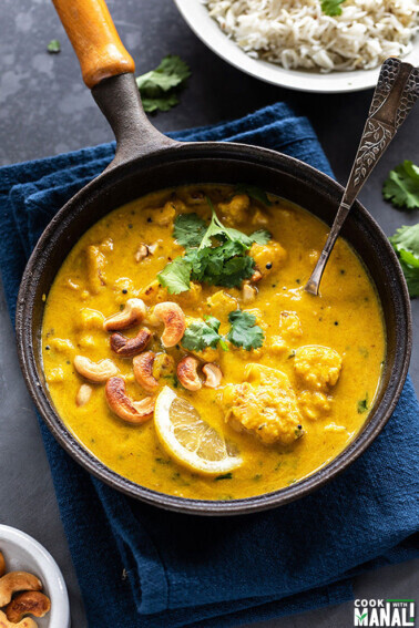 mango curry with cauliflower and cashews served in a black pan placed over blue napkin garnished with cilantro