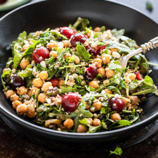 bowl of salad with cherry, quinoa, arugula, chickpea served with a spoon