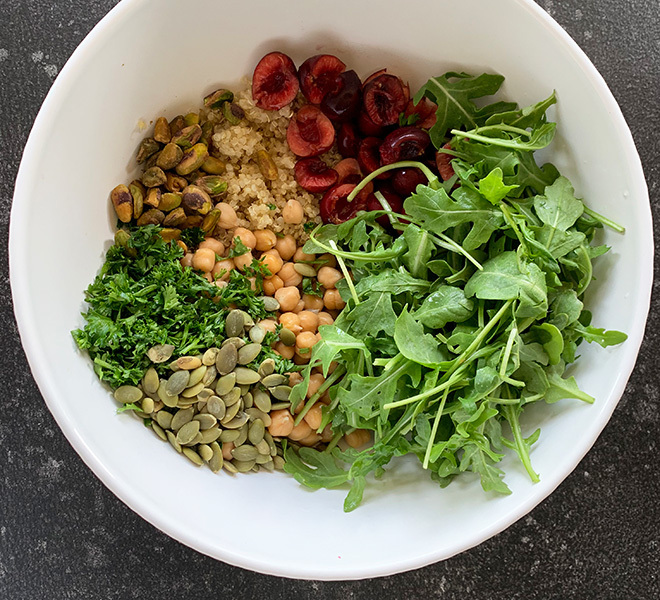 white bowl with cooked quinoa, chickpeas, arugula, cherries, parsley, pistachios