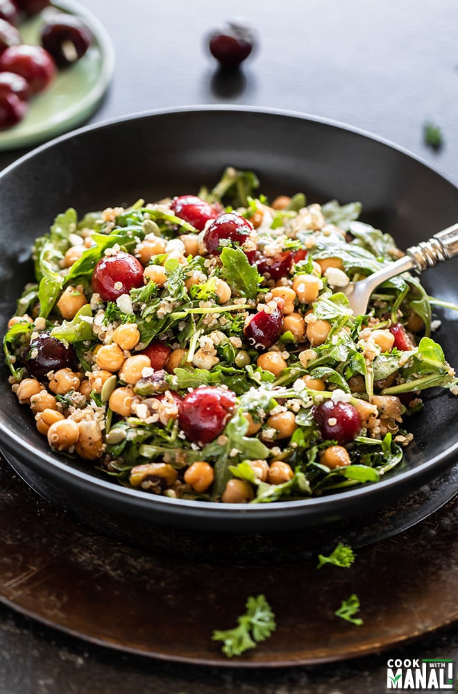 bowl of salad with cherry, quinoa, arugula, chickpea served with a spoon