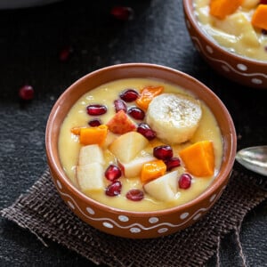 fruit custard served in a clay bowl, topped with sliced bananas, mangoes, apples