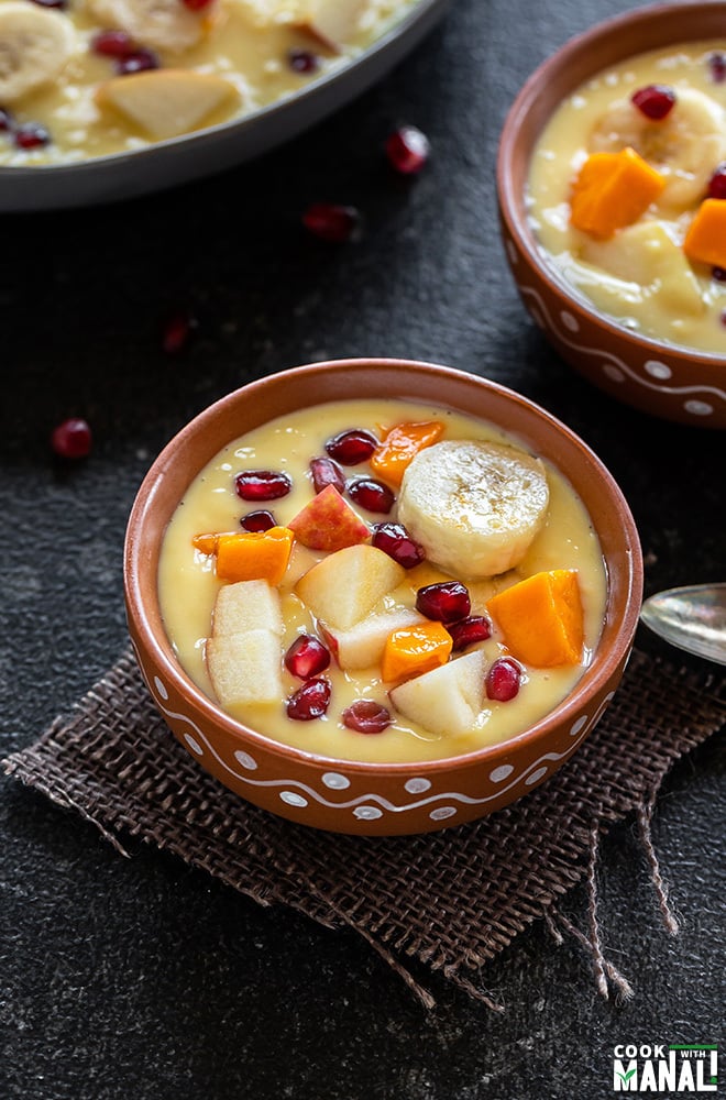 fruit custard served in a clay bowl, topped with sliced bananas, mangoes, apples