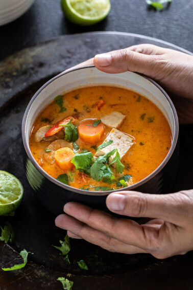 pair of hands holding a bowl of thai curry soup