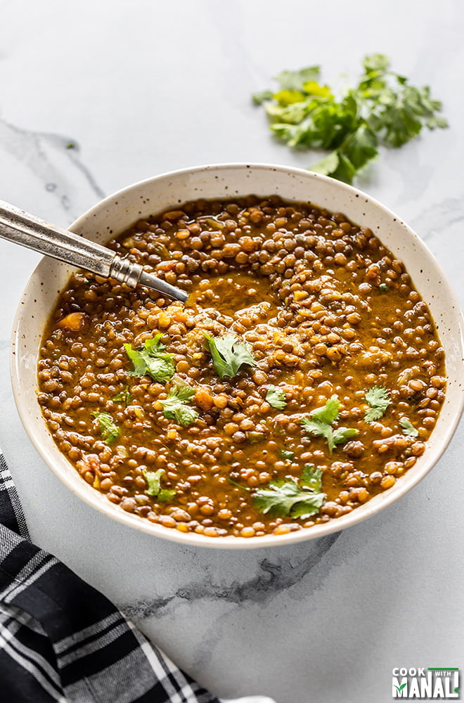 whole masoor dal served in a white bowl with a spoon, with some cilantro in the background