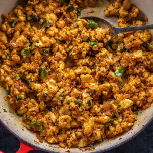 paneer bhurji served in a red pan and garnished with cilantro