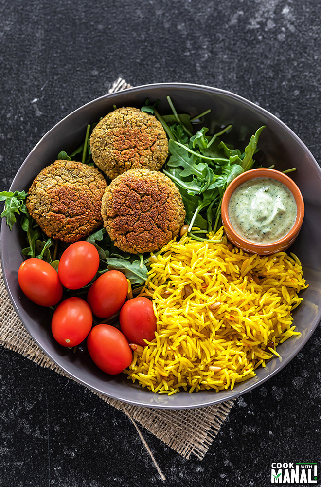 a bowl with falafel, saffron rice, greens, tomatoes and yogurt dip