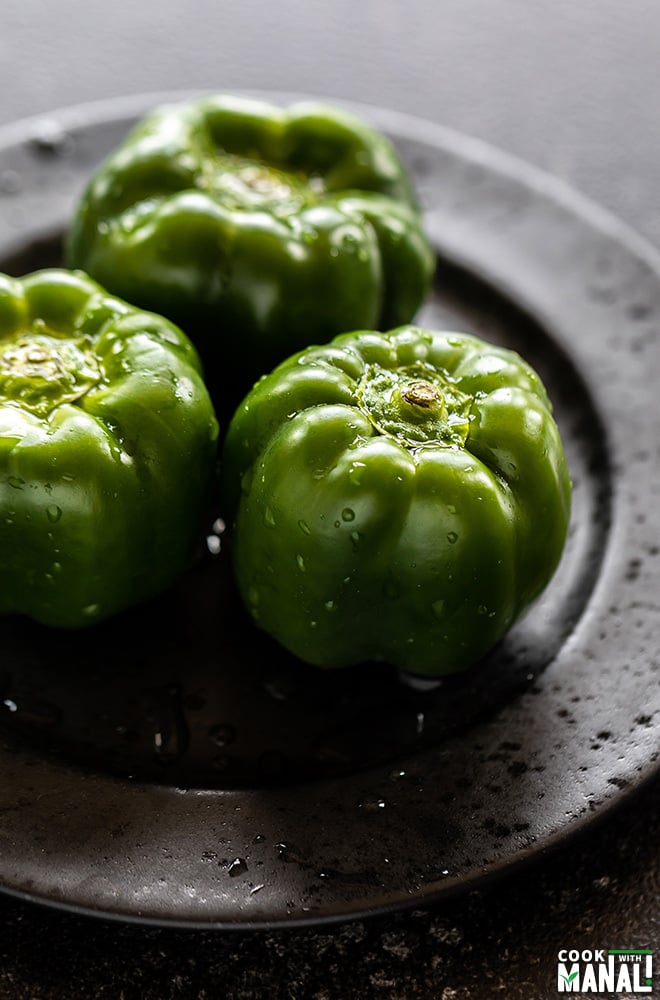 3 green bell peppers washed and arranged on a black plate