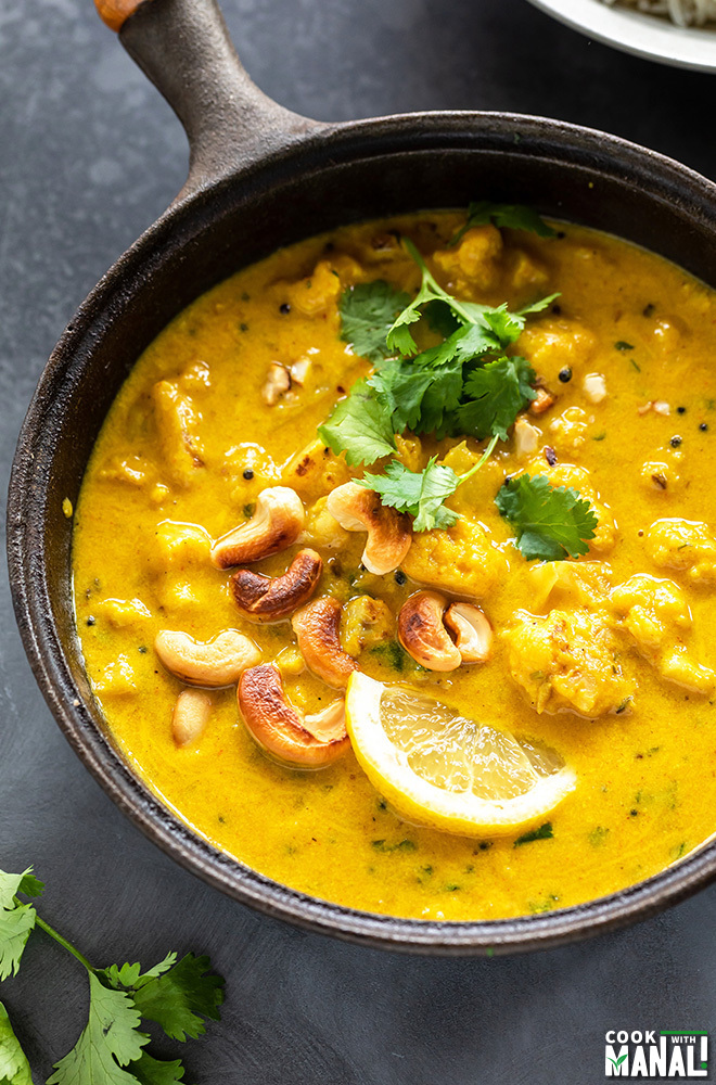 black pan filled with mango curry with cauliflower and cashews, garnished with cilantro