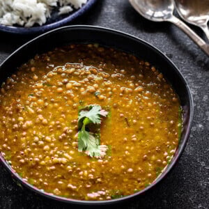 whole masoor dal served in a black bowl and garnished with cilantro