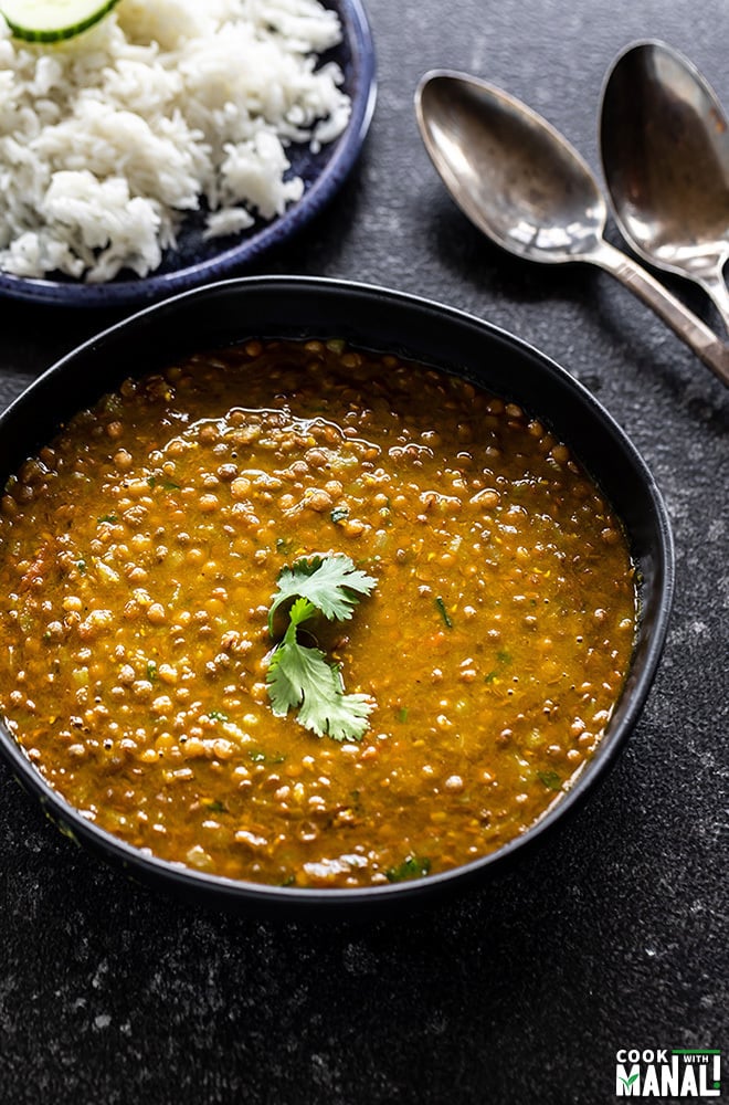 whole masoor dal served in a black bowl and garnished with cilantro