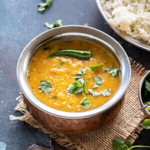 dal fry in a copper bowl garnished with green chili and cilantro with a plate of rice in the background