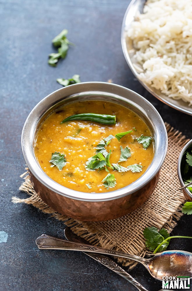 dal fry in a copper bowl garnished with green chili and cilantro with a plate of rice in the background