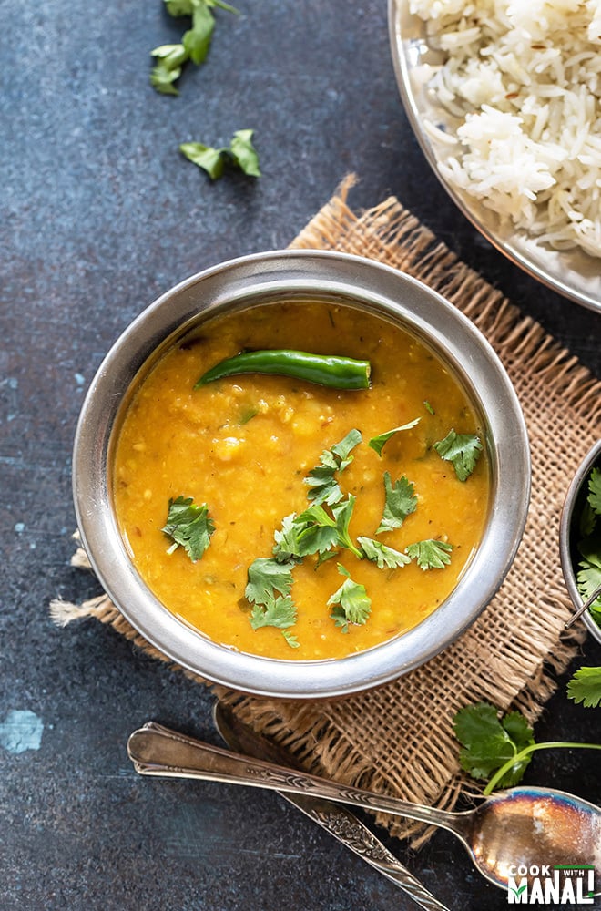 dal fry in a copper bowl garnished with green chili and cilantro with a plate of rice in the background