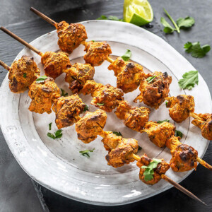three wooden skewers of mushroom tikka arranged on a white plate and garnished with cilantro