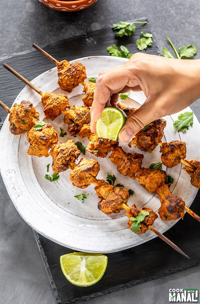 pair of hand squeezing lime juice on skewers of mushroom tikka arranged on a plate