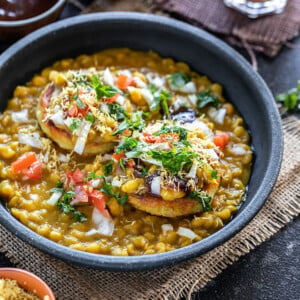 ragda patties served in a black bowl with a cup of chai and several bowls of chutney in the background and on the sides