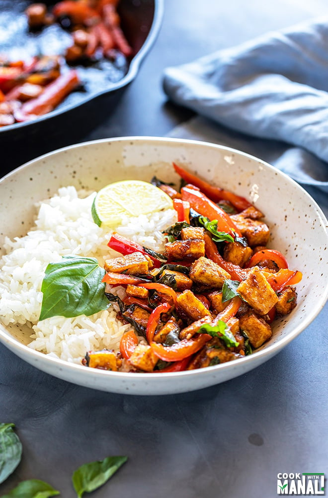 basil tofu stir fry served with jasmine rice in a white bowl garnished with lime wedge