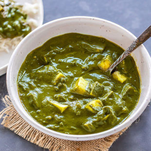 palak paneer served in a white bowl with a serving spoon