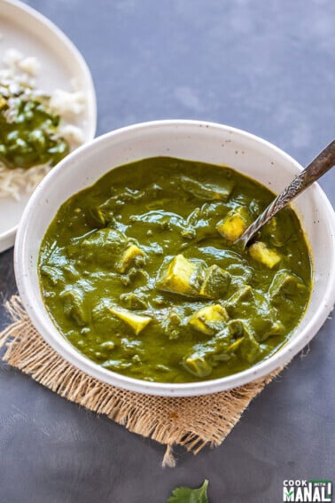 palak paneer served in a white bowl with a serving spoon