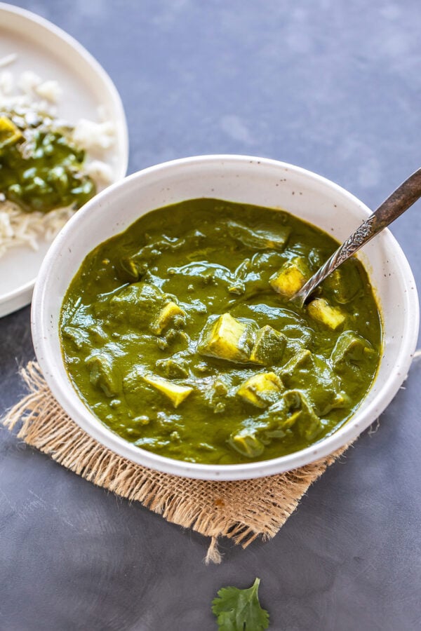 palak paneer served in a white bowl with a serving spoon