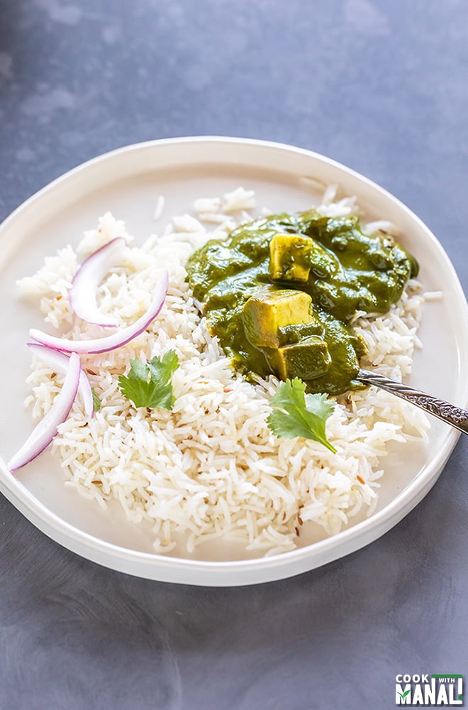 palak paneer served with basmati rice and sliced onions in a white plate