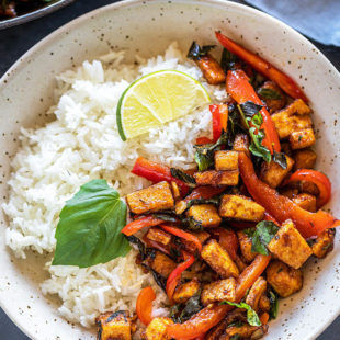 basil tofu stir fry served with jasmine rice in a white bowl garnished with lime wedge