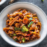 vegan drunken noodles served in a white bowl with forks placed in the background