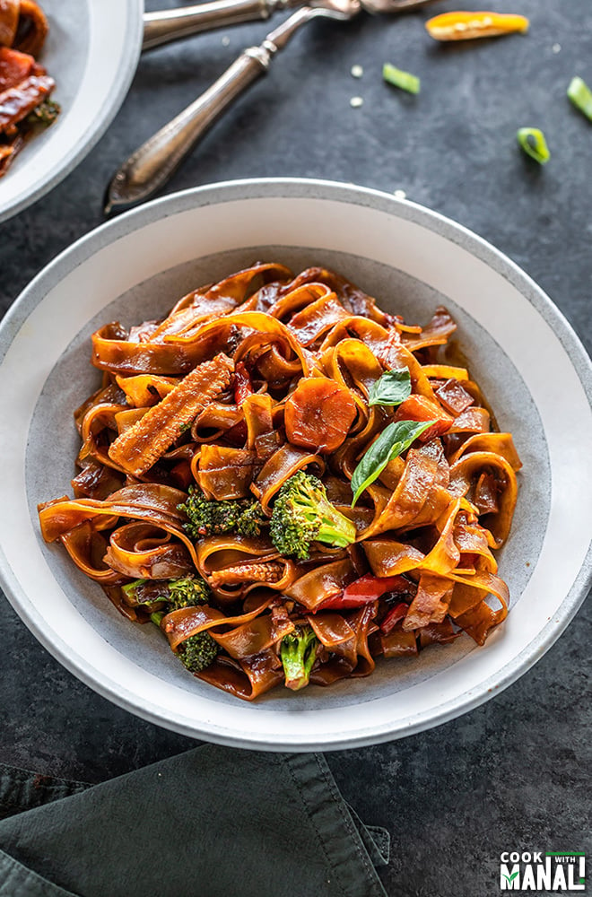 vegan drunken noodles served in a white bowl with forks placed in the background