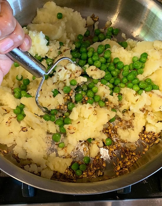 steel masher mashing potatoes with spices in a pan