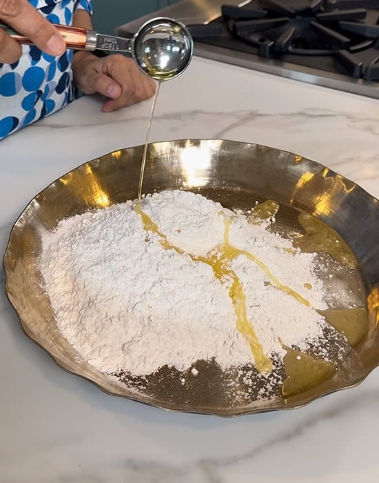 spoon adding oil to flour in a pan