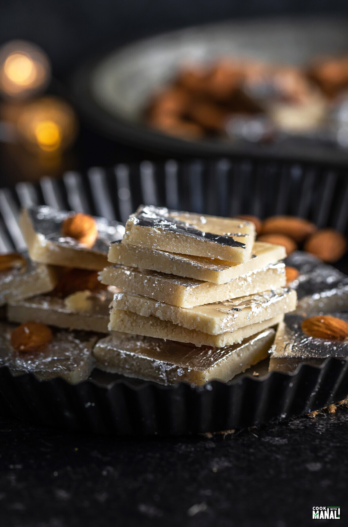 stack of badam burfi in a plate with some lights in the background