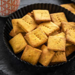 baked besan papdi in a black plate with a cup of coffee in the background