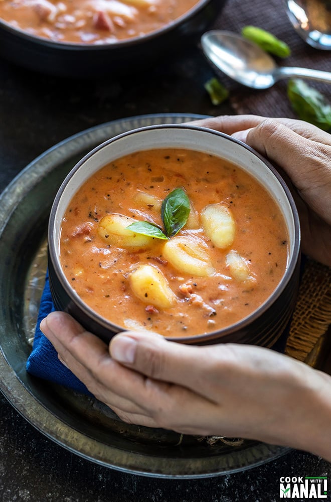 pair of hands holding a bowl of tomato gnocchi soup
