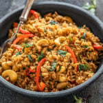 thai basil fried rice in a black bowl with a fork and few basil leaves scattered around
