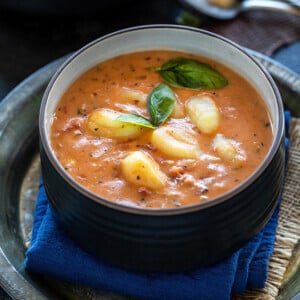 tomato gnocchi soup in a black bowl garnished with basil and some spoons in the background